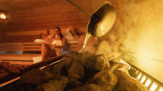 Aufguss auf die heißen Steine, im Hintergrund Gäste in der Sauna